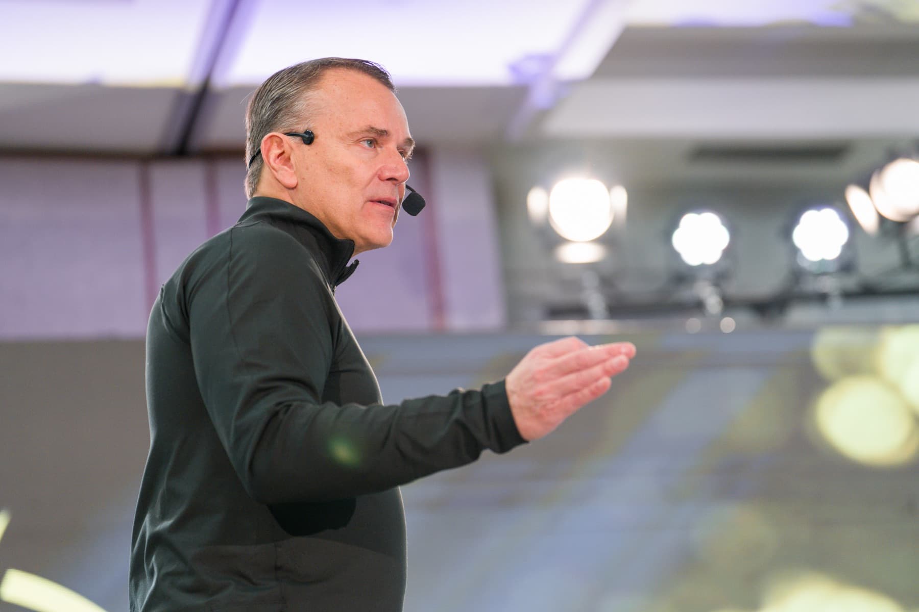 Sean Callagy on stage mid-presentation, hand extended toward the audience